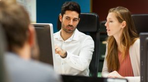 Two people talking in front of a computer screen.